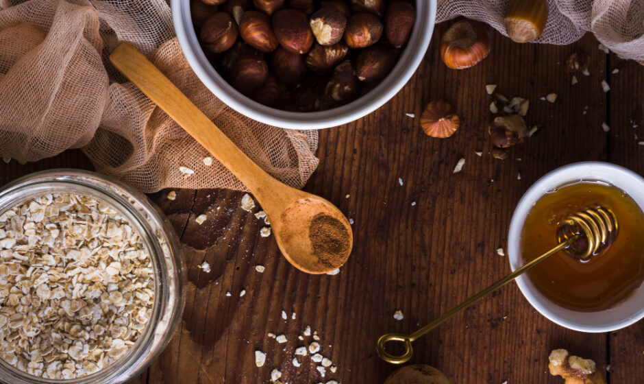 On a wooden table, hazelnuts, oats, and honey are arranged with a spoon, emphasizing premium honey and finest coffee beans.