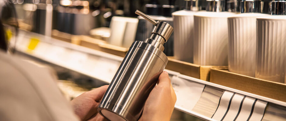 A woman showcases a bottle of premium stainless steel soap in a store, with food preservation boxes in the background.