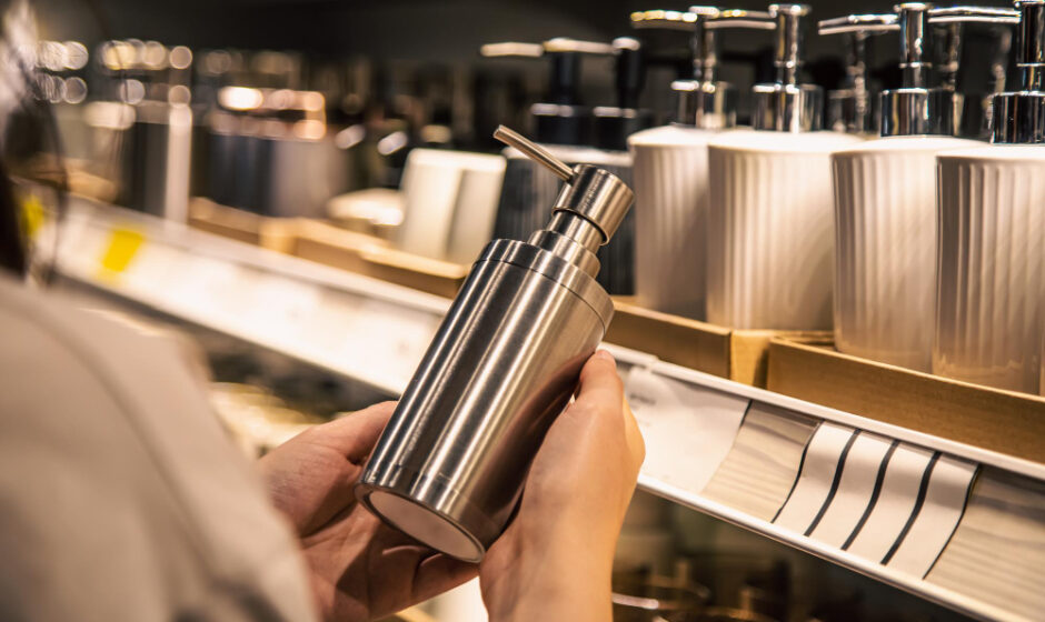 A woman showcases a bottle of premium stainless steel soap in a store, with food preservation boxes in the background.