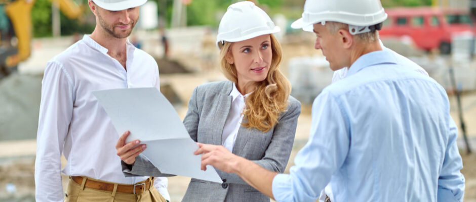 Three individuals in hard hats engage in discussion at a construction site, emphasizing safety and collaboration in artisan contracting.