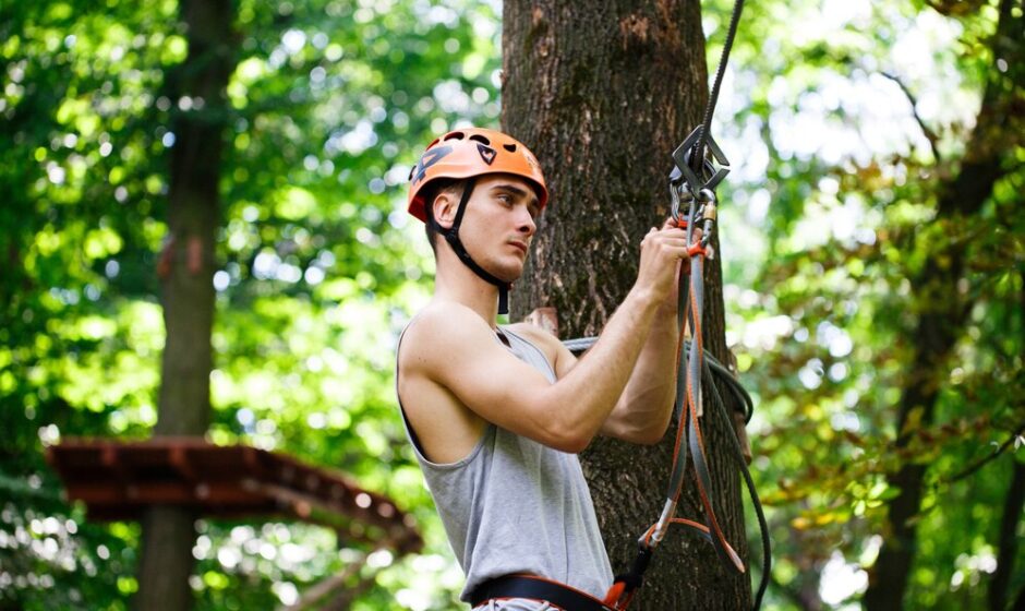 A man in safety gear and a helmet experiences the excitement of zip lining, representing innovative climbing and twisting adventures.