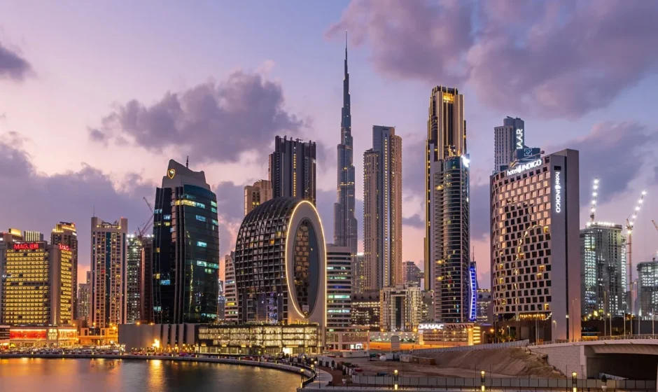 Skyline of Dubai at dusk, featuring modern high-rise buildings including the iconic Burj Khalifa in the center, uniquely designed skyscrapers like The Opus by Zaha Hadid with a central void, and illuminated waterfront properties reflecting on the calm water below.